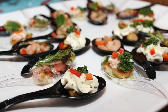 Cucchiaini con finger food gourmet colorati, disposti su piatto bianco