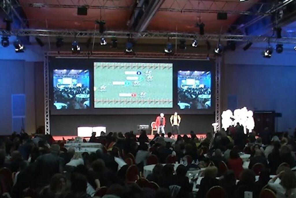 Palco allestito per quiz show aziendale con pubblico e maxi schermi
