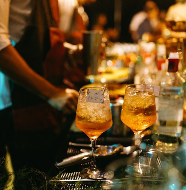 Due cocktail spritz su bancone da bar con luci calde, pronti per evento con delitto