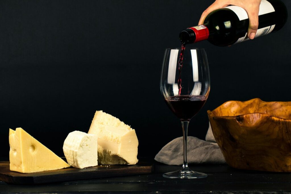 Vino rosso versato nel calice con formaggi su tagliere